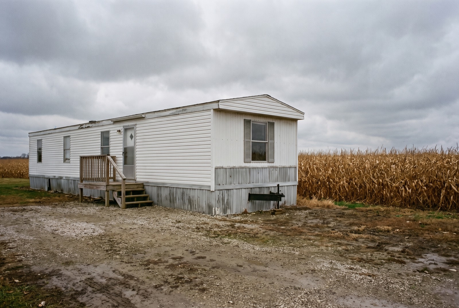A single-wide manufactured home with skirting and a small deck beside a field